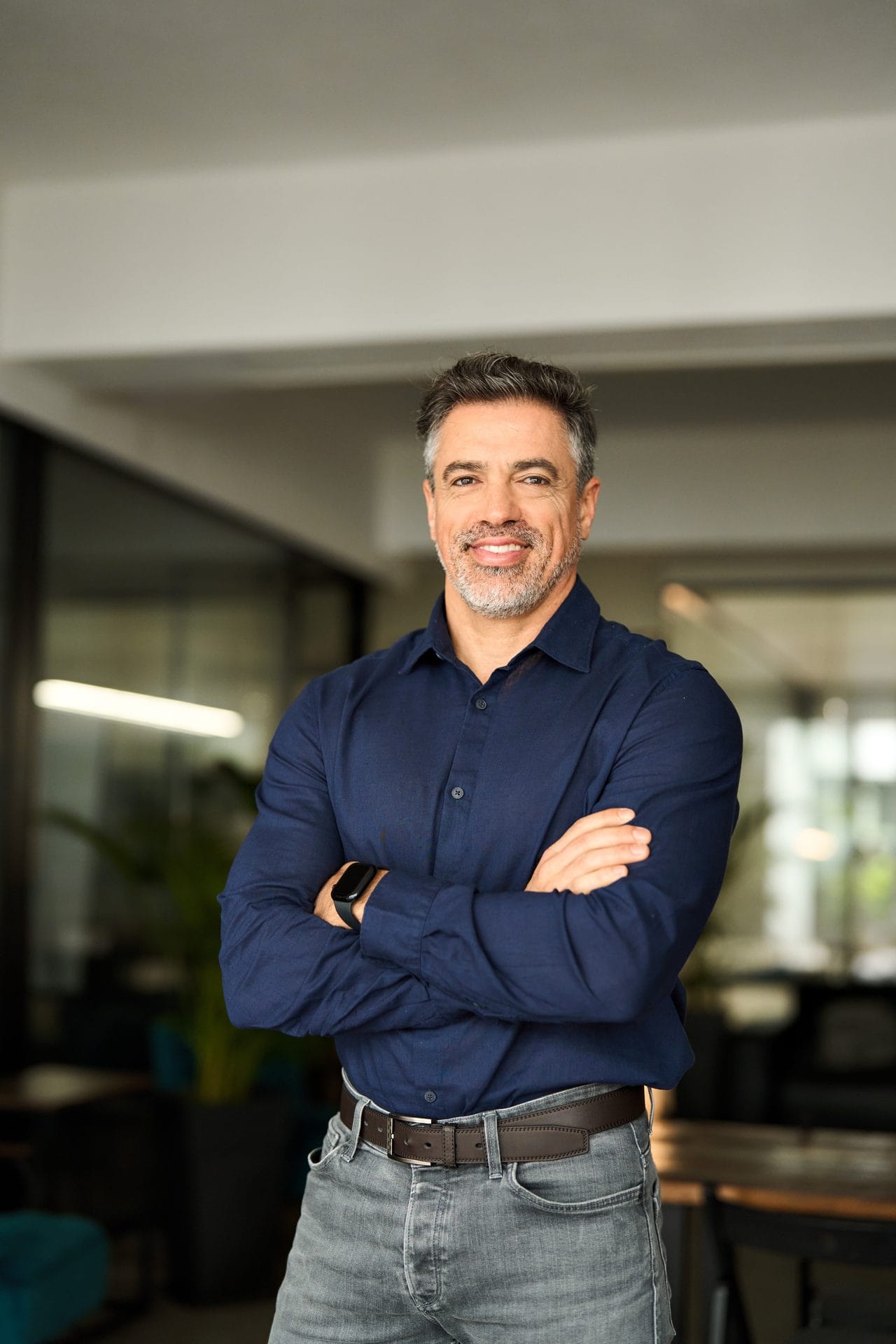 Confident man in a navy shirt standing with his arms crossed in a modern office